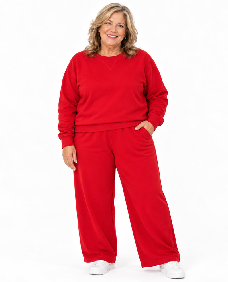 A woman modeling a matching red sweatshirt and wide-leg sweatpants set against a plain white studio background.