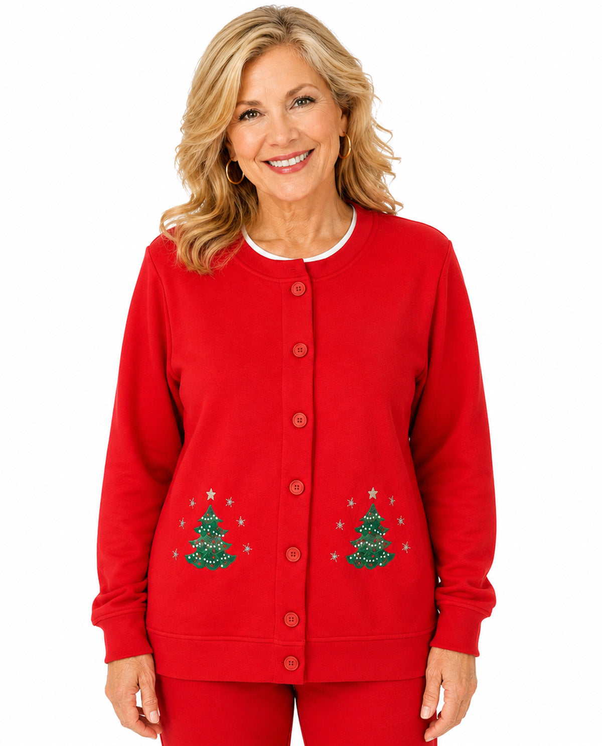A smiling woman wearing a bright red button-front cardigan with embroidered green Christmas trees and small gold stars on the front, paired with matching red pants, against a plain white background.