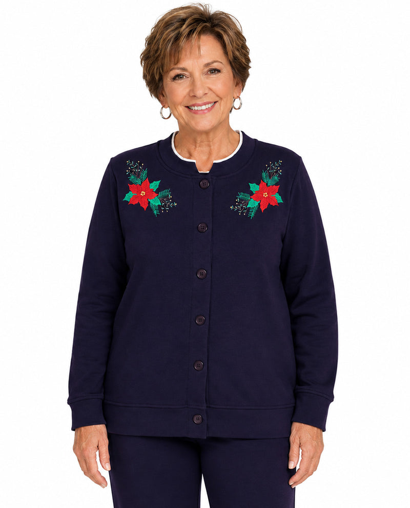 A smiling woman with short brown hair models a navy blue button-front cardigan with red and green floral embroidery on the chest, paired with matching navy pants, against a plain white background.