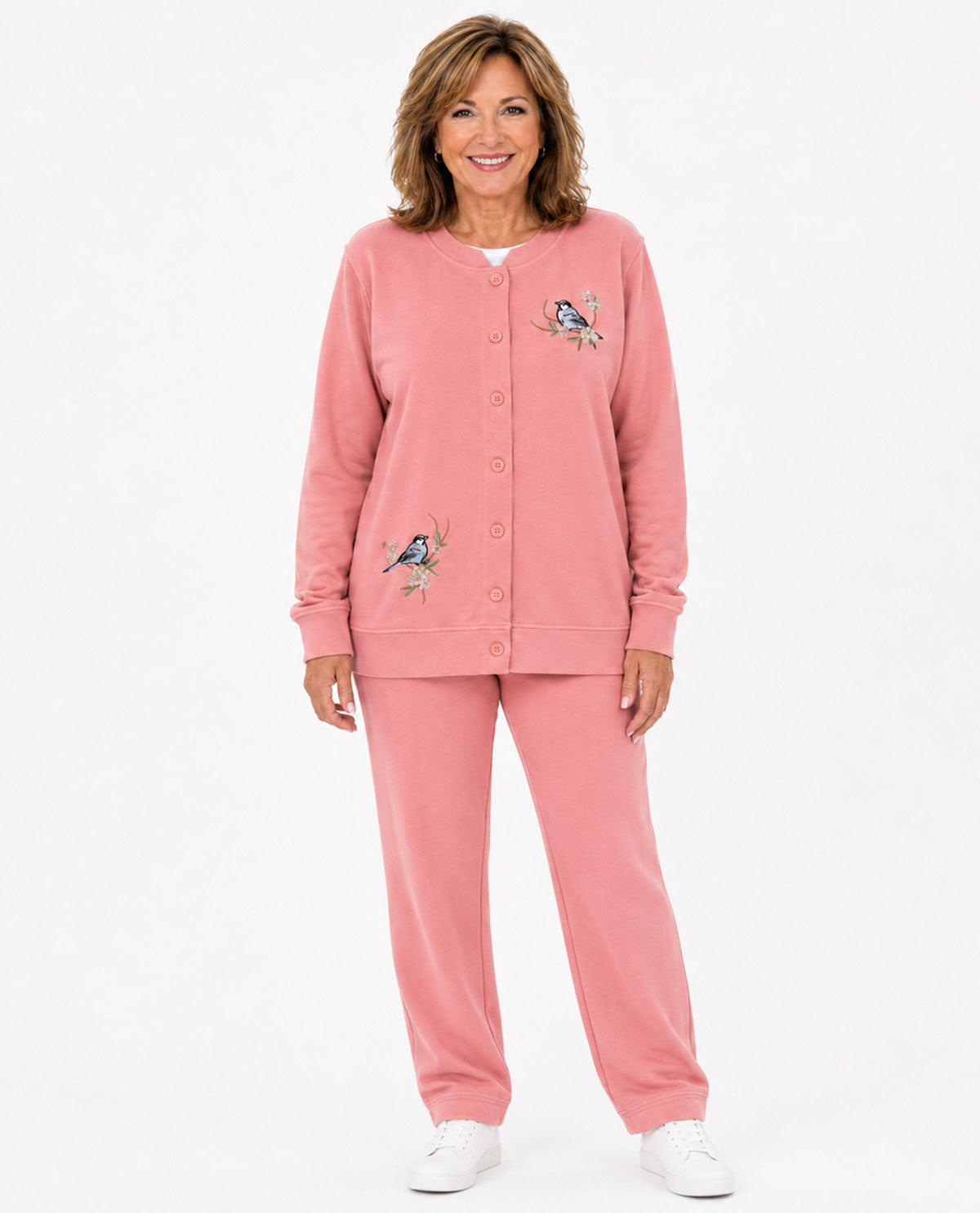 A woman modeling a matching pink lounge set consisting of a button-front cardigan and sweatpants, featuring embroidered bird designs on the chest and left leg, against a plain white studio background.