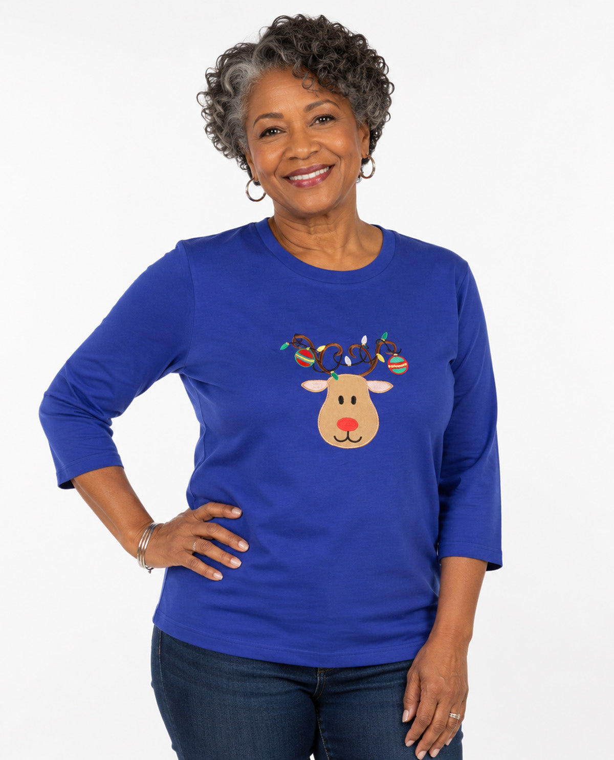 Person wearing a blue top with a reindeer wearing ornaments with a white background