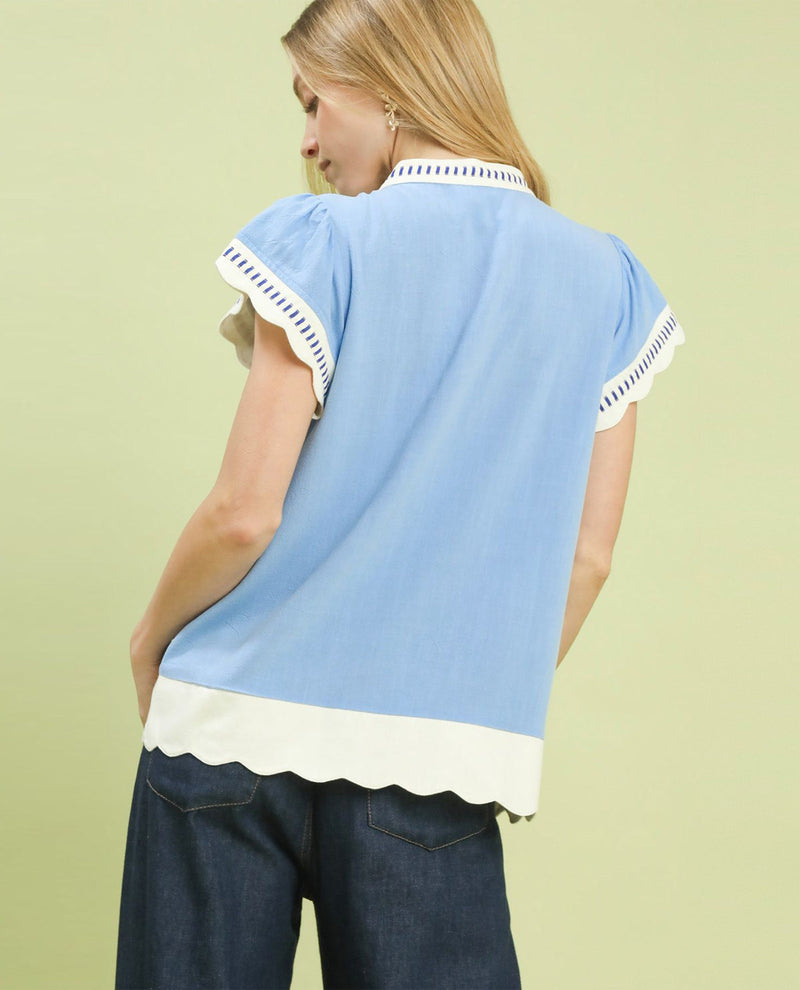 Woman wearing a light blue blouse with white trim on a plain background