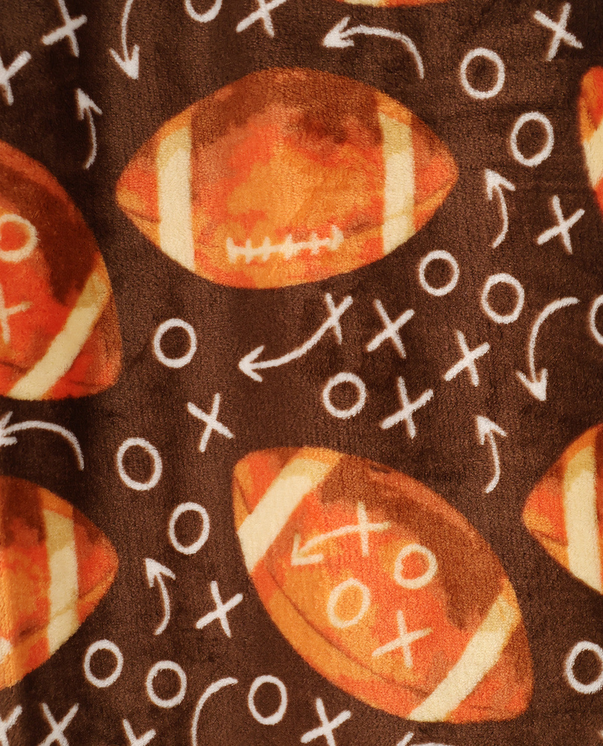 Close-up of a brown fabric with a repeating football and play-calling pattern. The design features orange and white footballs with white markings, surrounded by white arrows, circles, and crosses on a dark brown background.