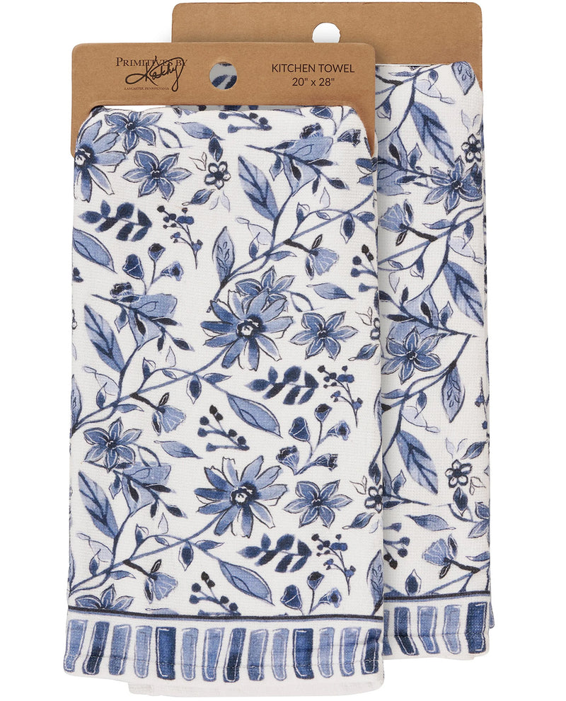 Two white kitchen towels with a blue floral pattern and striped fringed edges, hanging from kraft paper hangers labeled Preset by Preset.