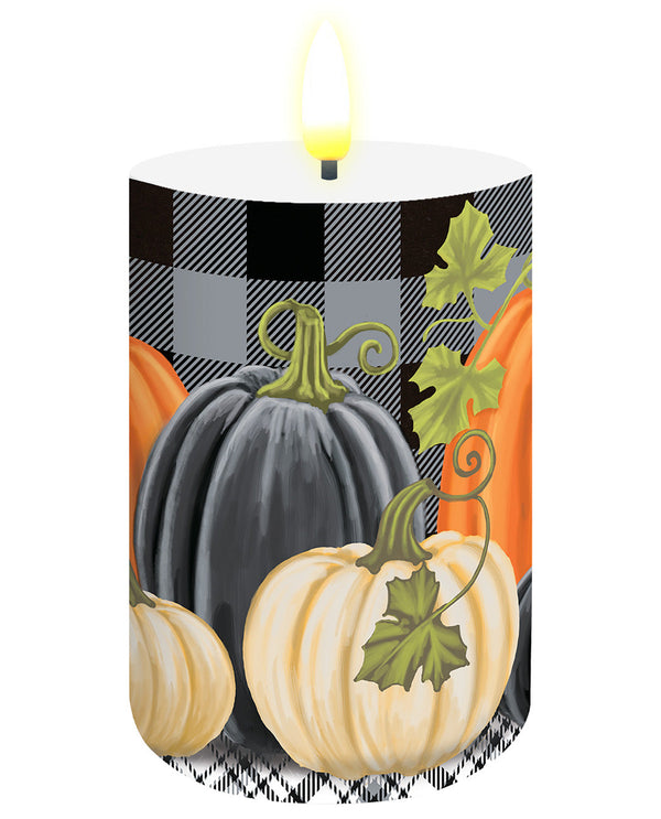 A lit pillar candle with a printed autumn design featuring pumpkins, a black-and-gray buffalo plaid pattern, and green leaves, shown on a plain white background.