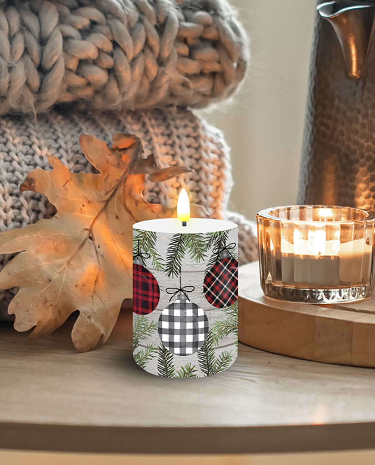Decorative candle with festive pattern on a wooden surface with another candle and autumn leaves.