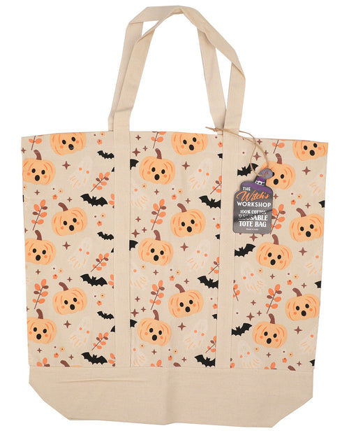 A canvas tote bag with a Halloween pattern featuring orange pumpkins, black bats, and orange leaves on a cream background, with a hanging tag that reads 'The Witch's Workshop'.