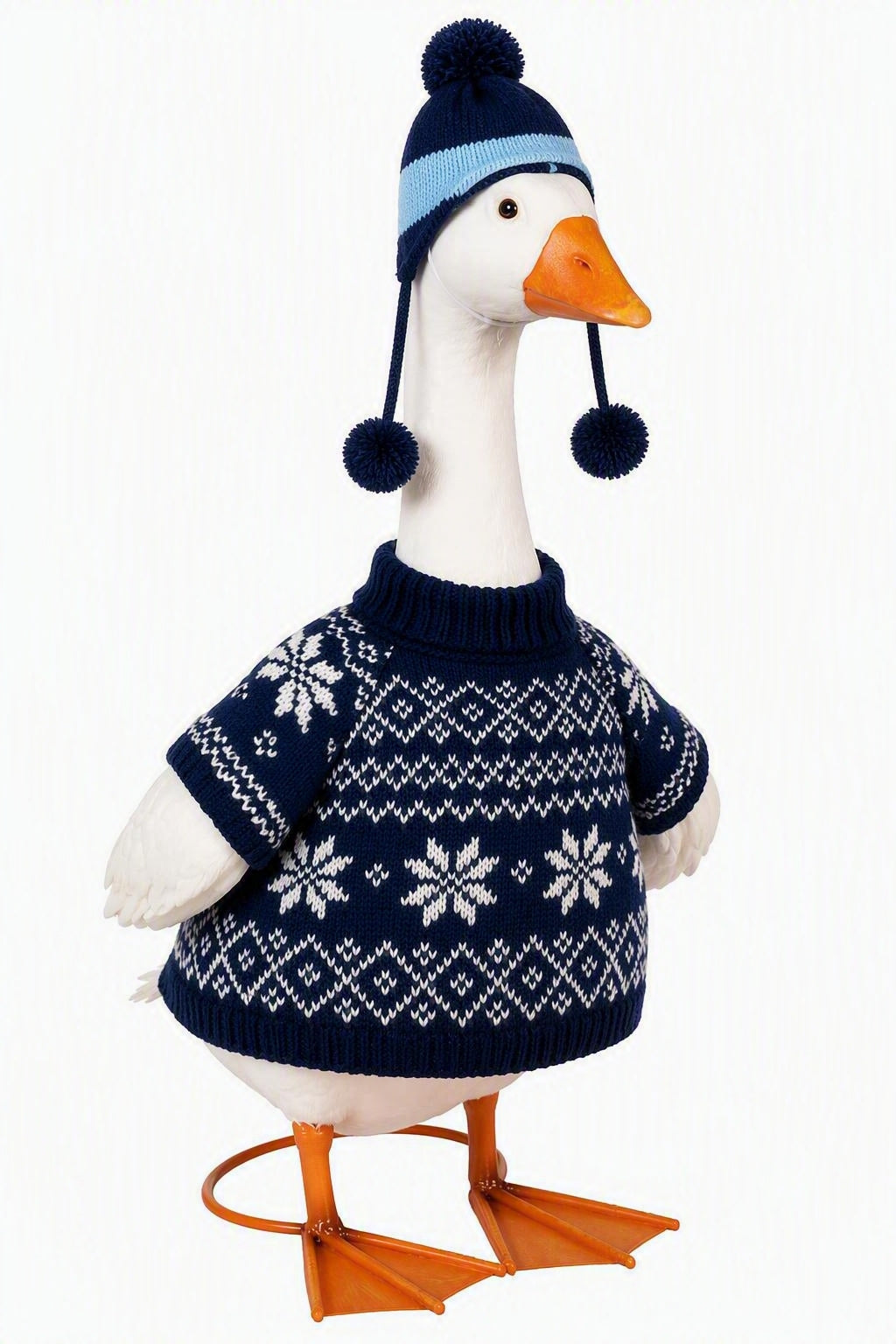 A white goose decoration wearing a navy blue and light blue knit beanie with pom-poms and a matching navy blue sweater with white snowflake patterns, standing on an orange plastic webbed base against a white background.
