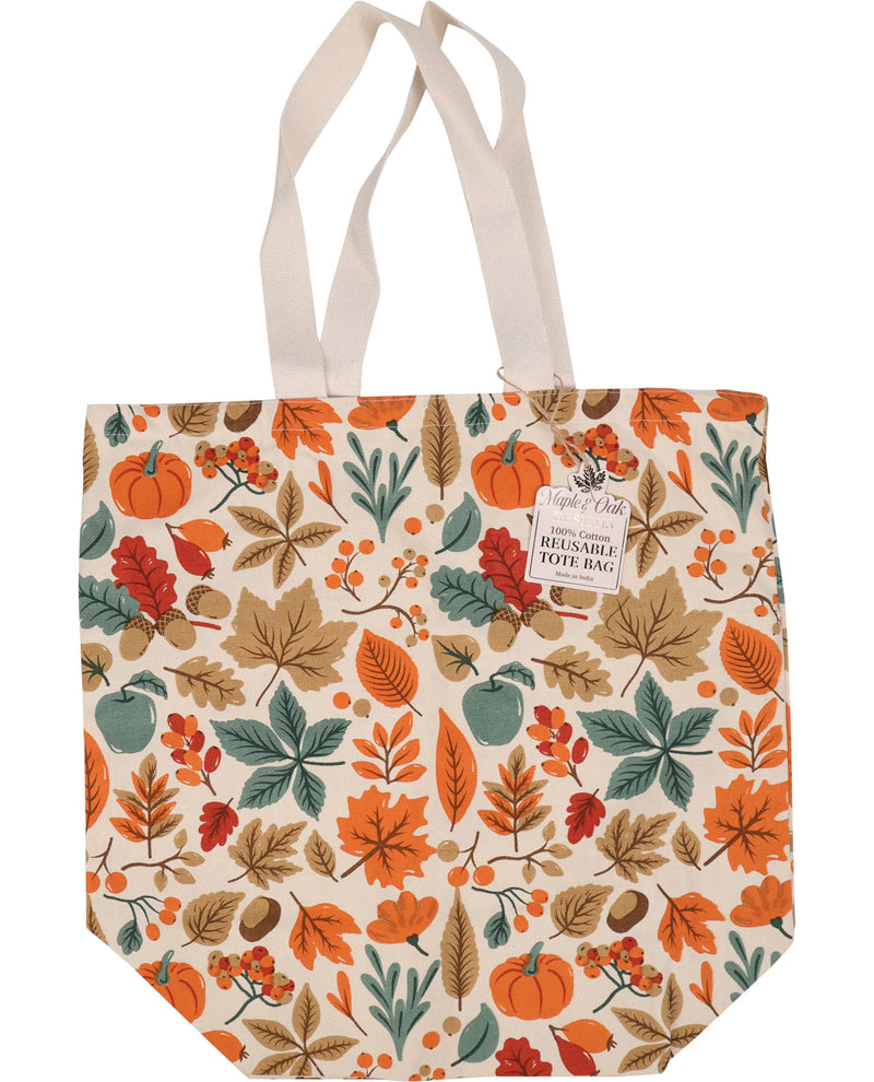 A canvas tote bag with a cream background and an all-over autumn leaf, pumpkin, acorn, and berry pattern in orange, brown, teal, and red. It has two cream fabric handles and a hanging paper tag that reads 'A little bit of truth handmade reusable tote bag'.