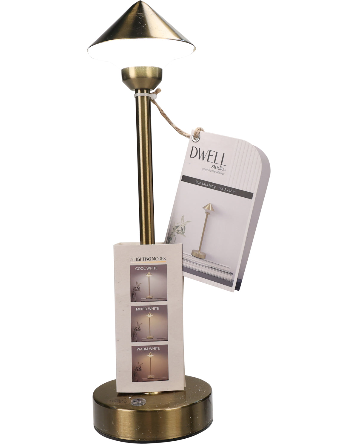 A brass table lamp with a tapered shade, slim stem, and round base, shown on a white background with a hanging product tag and a small display card. The tag reads DWELL Lighting.