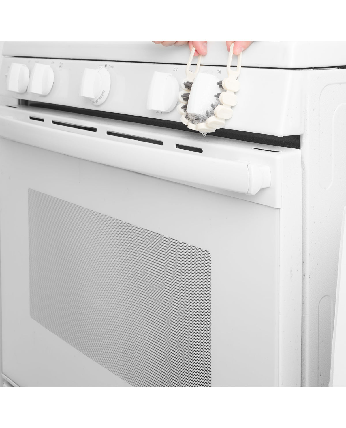 A white electric range oven with control knobs on top and a decorative white floral garland hanging from the handle area, with two hands visible at the top.