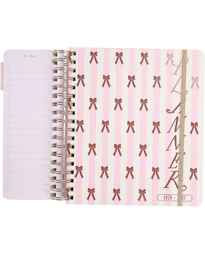 Pink planner with bow pattern and gold spiral binding on a white background