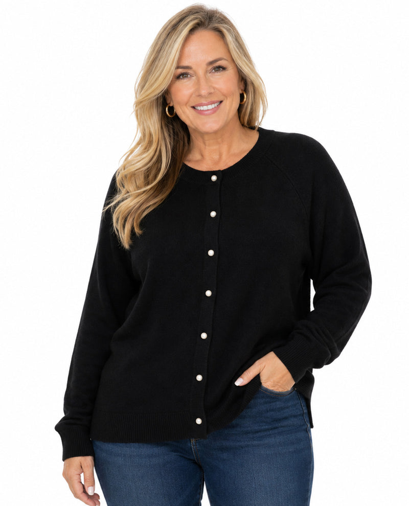 A smiling blonde woman wearing a black long-sleeve button-front cardigan sweater with white buttons and blue jeans, photographed against a plain white studio background.