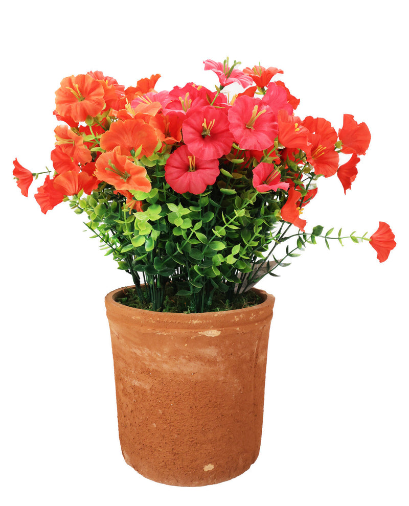 An artificial flower arrangement featuring vibrant orange, red, and pink blossoms with green foliage, presented in a textured terracotta-colored plastic pot against a plain white background.