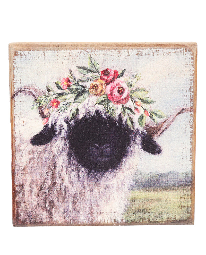 Decorative wall art of a sheep with floral crown on a wooden frame.
