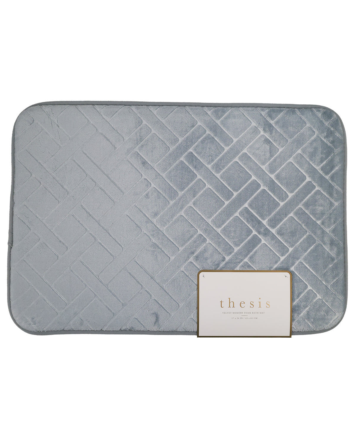 A light gray quilted bath mat with a geometric pattern, featuring a small white brand tag that reads 'thesis' on a plain white background.