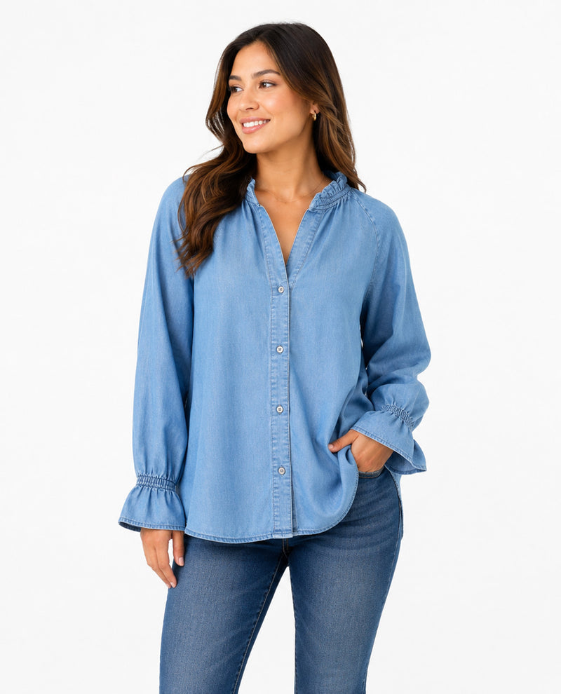A woman wearing a light blue long-sleeve button-up shirt with ruffled cuffs and collar, paired with blue jeans, against a plain white background.