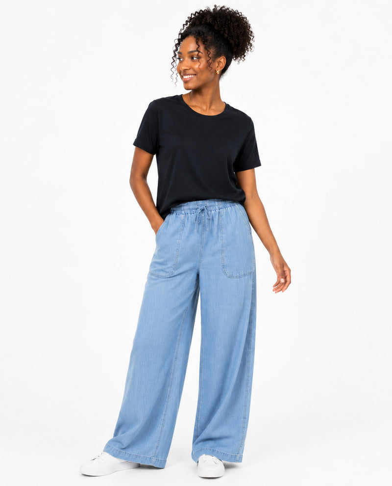 A woman modeling a black short-sleeve t-shirt and light blue wide-leg denim pants against a plain white studio background.