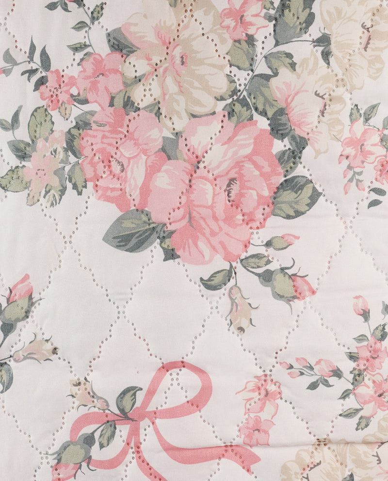 A close-up of a quilted fabric featuring a vintage floral pattern with pink and cream roses, green leaves, and a stitched diamond lattice design.