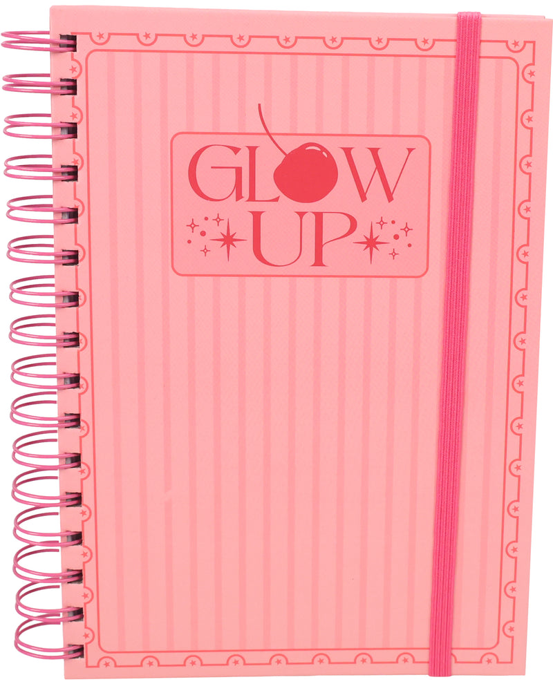 A pink spiral-bound notebook with a matching pink elastic closure band. The cover features a subtle vertical ribbed texture, a decorative border pattern, and the words 'GLOW UP' printed in the center with a cherry graphic.