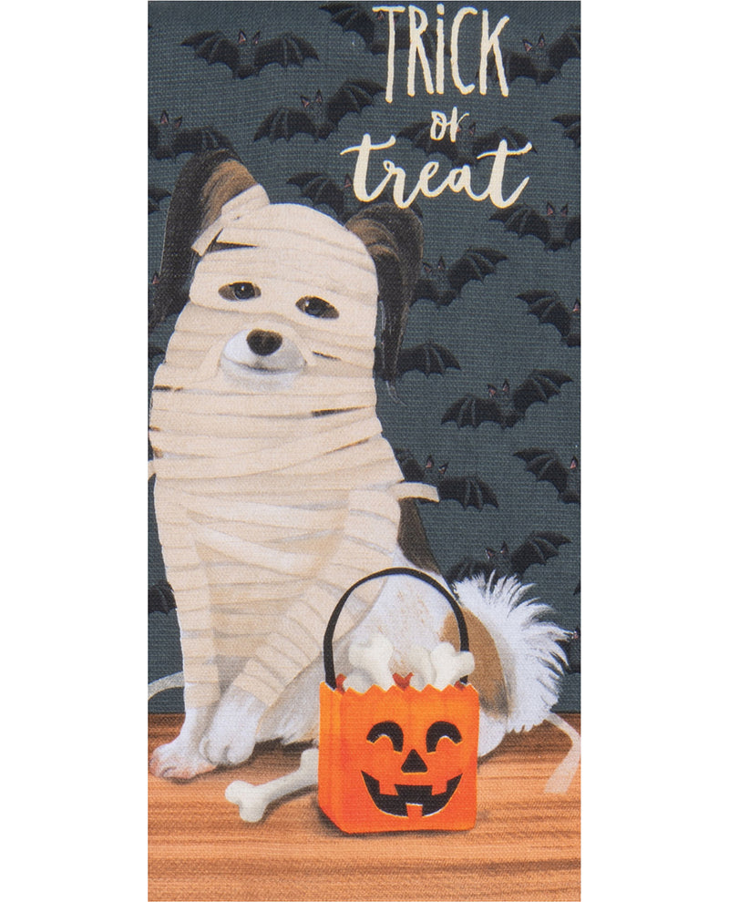 A rectangular decorative print or textile featuring a mummy-wrapped dog sitting beside an orange jack-o'-lantern trick-or-treat bucket, with the words “Trick or Treat” at the top and bats on a dark background.