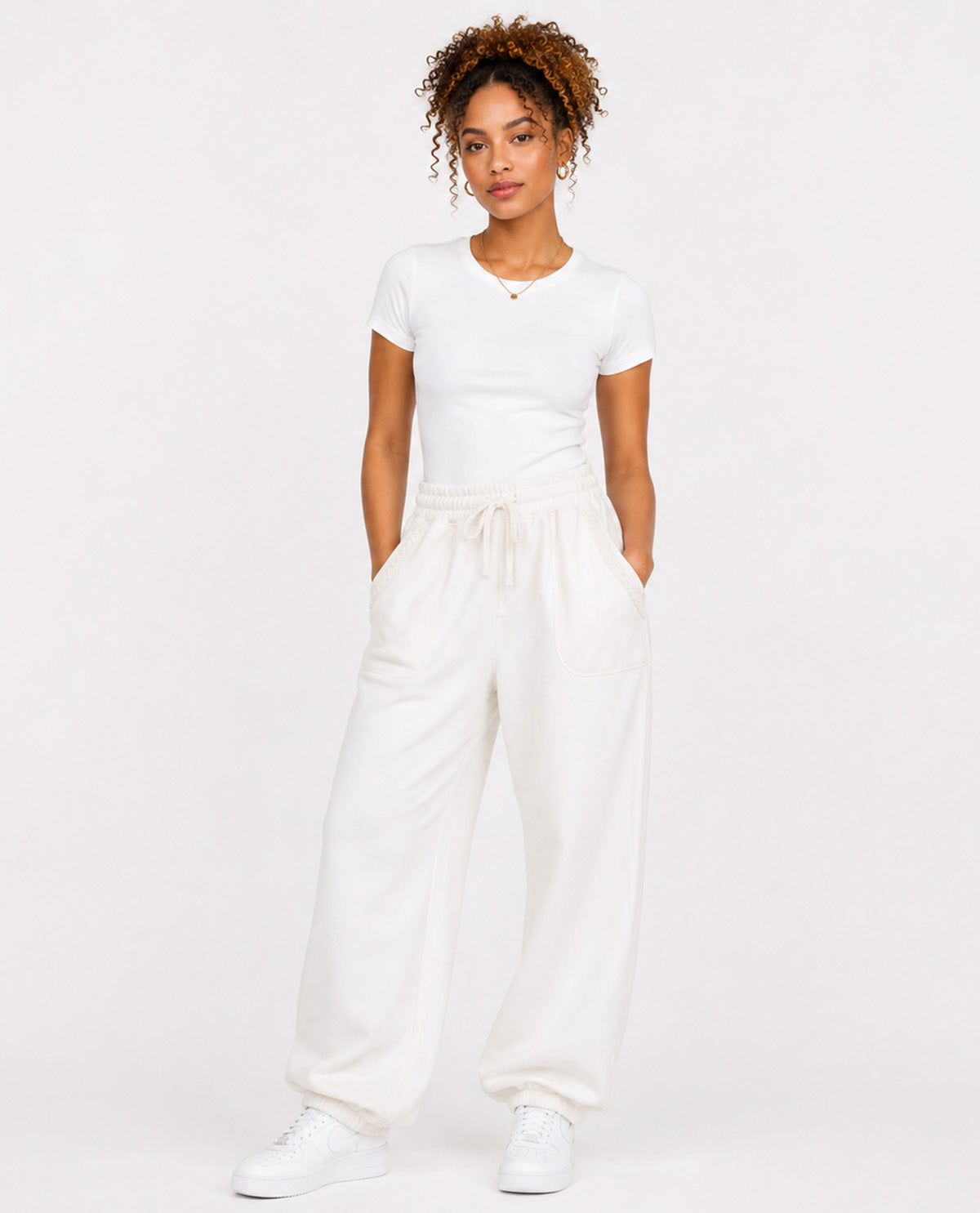 A woman modeling a white short-sleeve crewneck t-shirt and matching white wide-leg drawstring sweatpants, paired with white sneakers, against a solid white studio background.