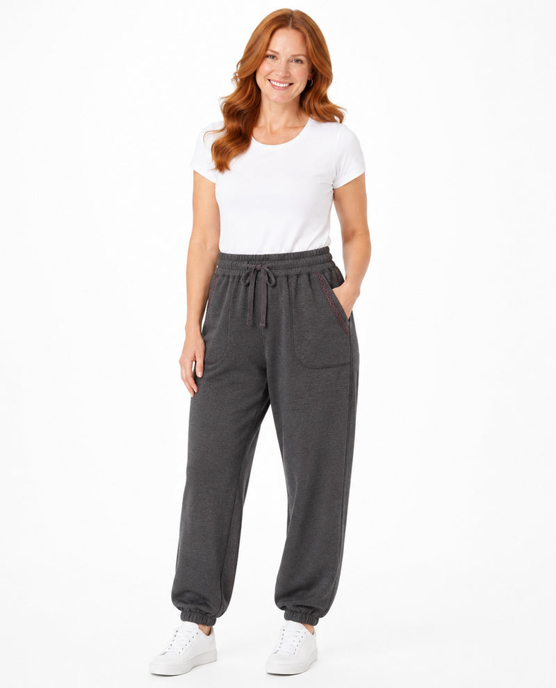 A woman modeling dark gray jogger sweatpants with a drawstring waist and side pockets, paired with a white t-shirt and white sneakers, against a plain white background.