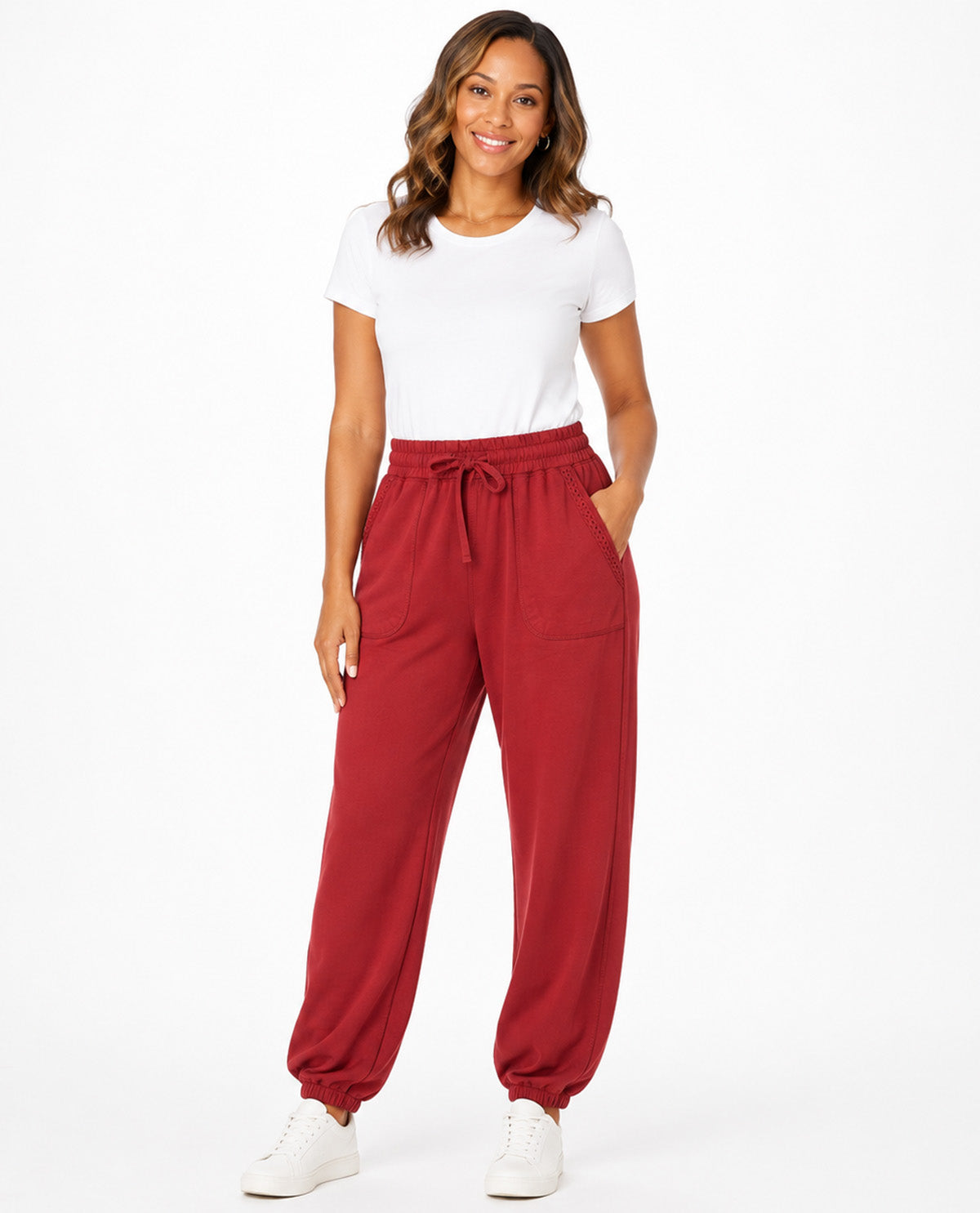 A woman modeling a pair of red drawstring jogger pants with a white t-shirt and white sneakers, standing against a plain white studio background.