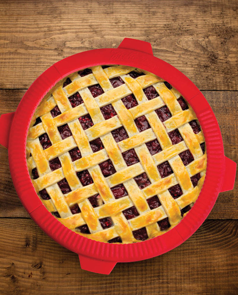 Pie with a lattice crust in a red silicone pie shield on a wooden surface