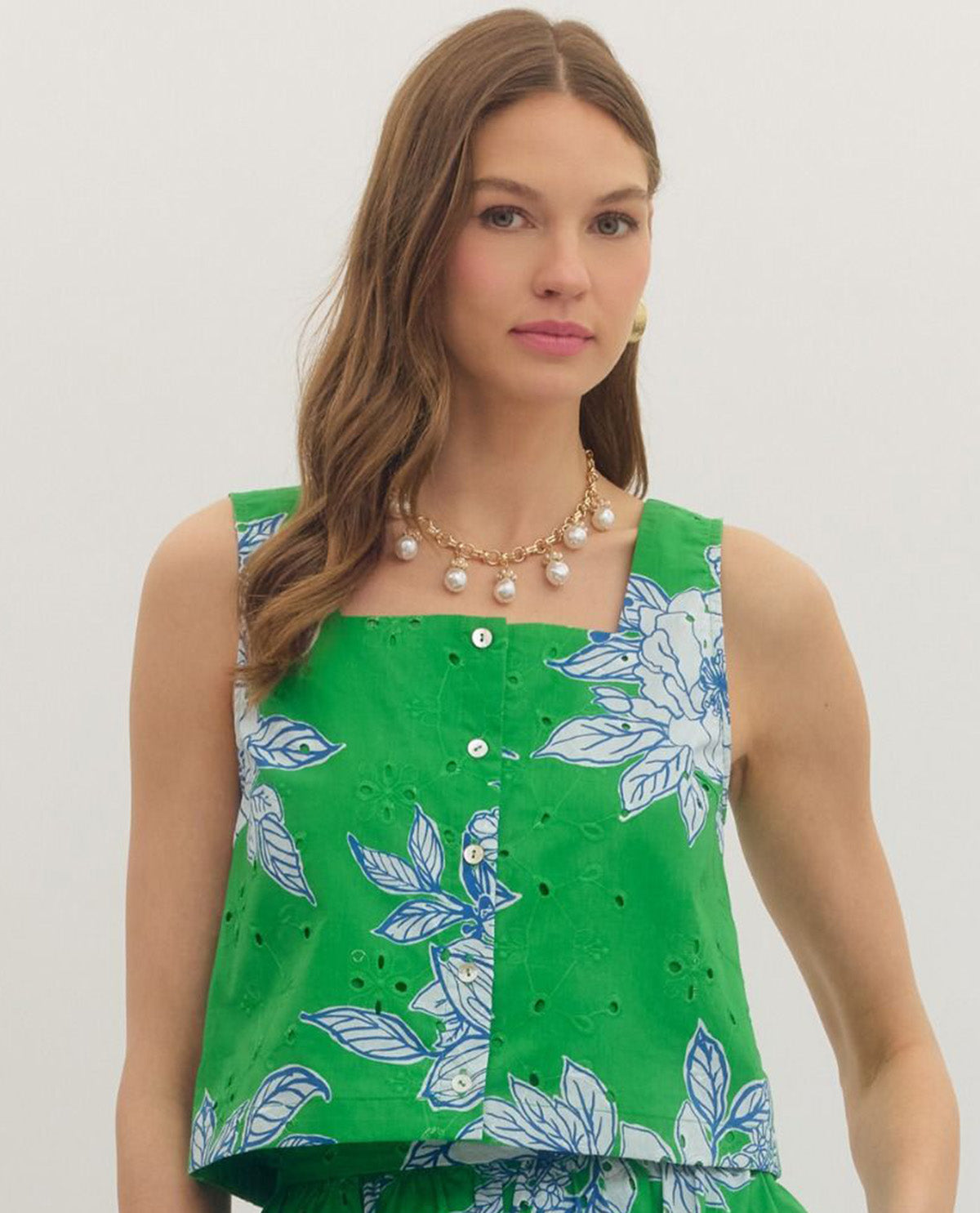 Woman wearing a green sleeveless top with floral pattern on a plain background