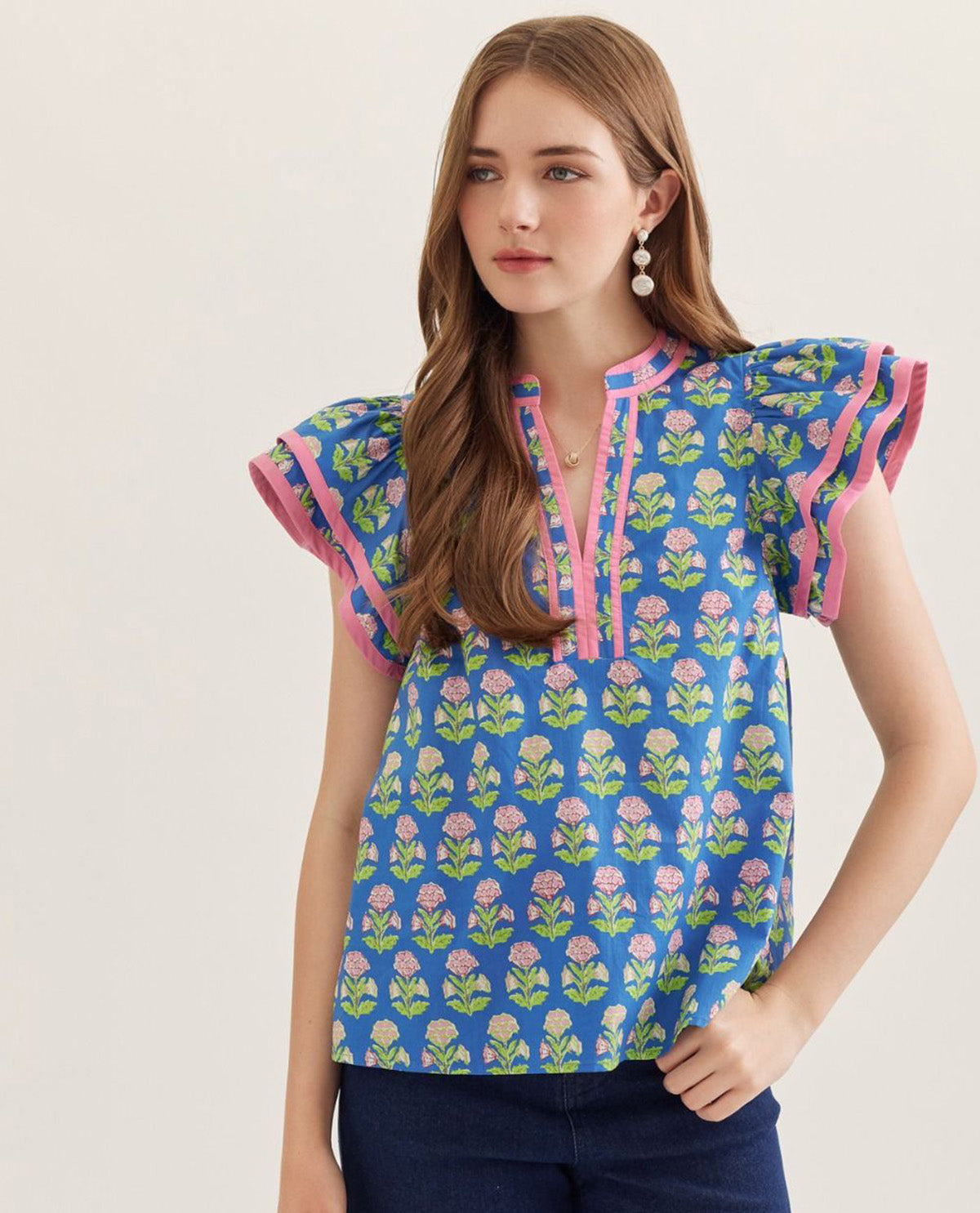 Woman wearing a blue floral patterned top with pink accents on a plain background