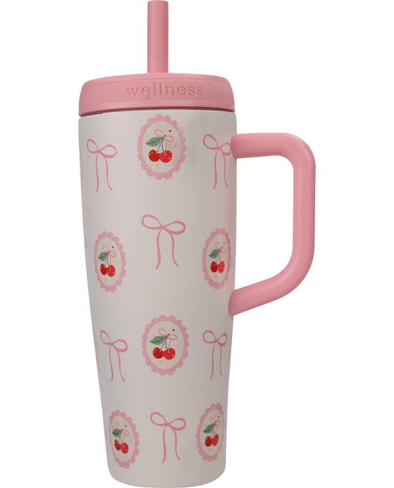 A tall insulated travel tumbler with a pink handle, pink lid, and pink straw. The tumbler body is white with a repeating pattern of pink bows and cherries inside pink scalloped circles.