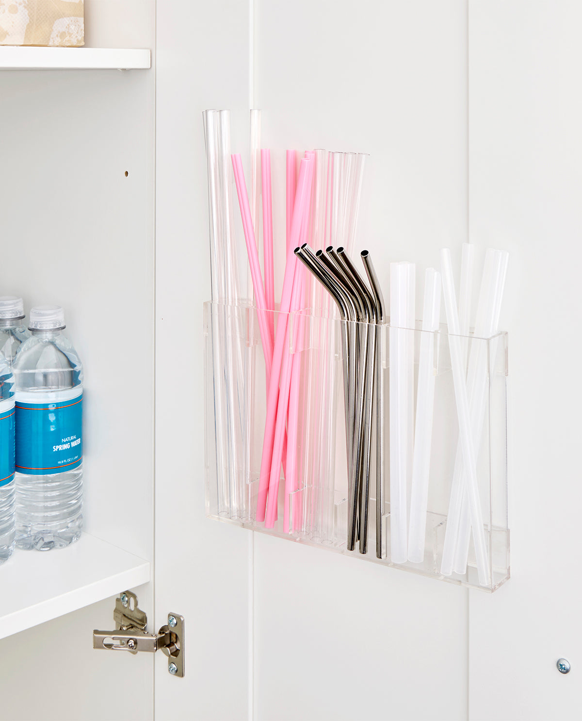 Clear straw holder with pink, black, and white straws inside a cabinet.