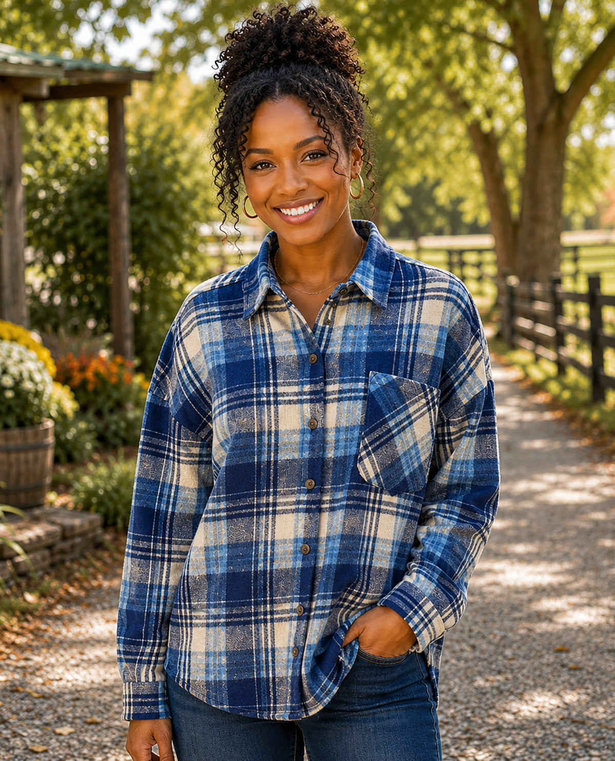 A woman wearing a blue and beige plaid button-up flannel shirt, standing on a gravel path in an outdoor garden setting.