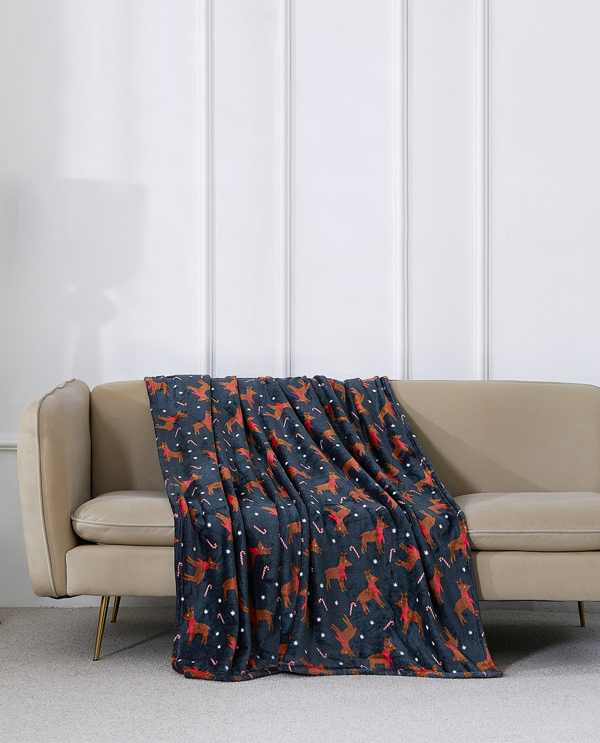 A navy blue throw blanket with a red and white dog pattern is draped over a beige sofa in a modern living room setting.