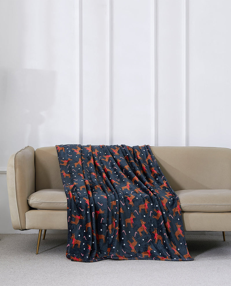 A navy blue throw blanket with a red and white dog pattern is draped over a beige sofa in a modern living room setting.