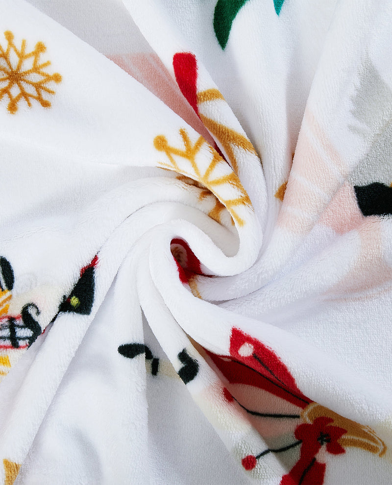 A close-up of a white plush fabric with a colorful holiday print, including red and gold snowflakes, green leaves, and black accents, arranged in a spiral drape.
