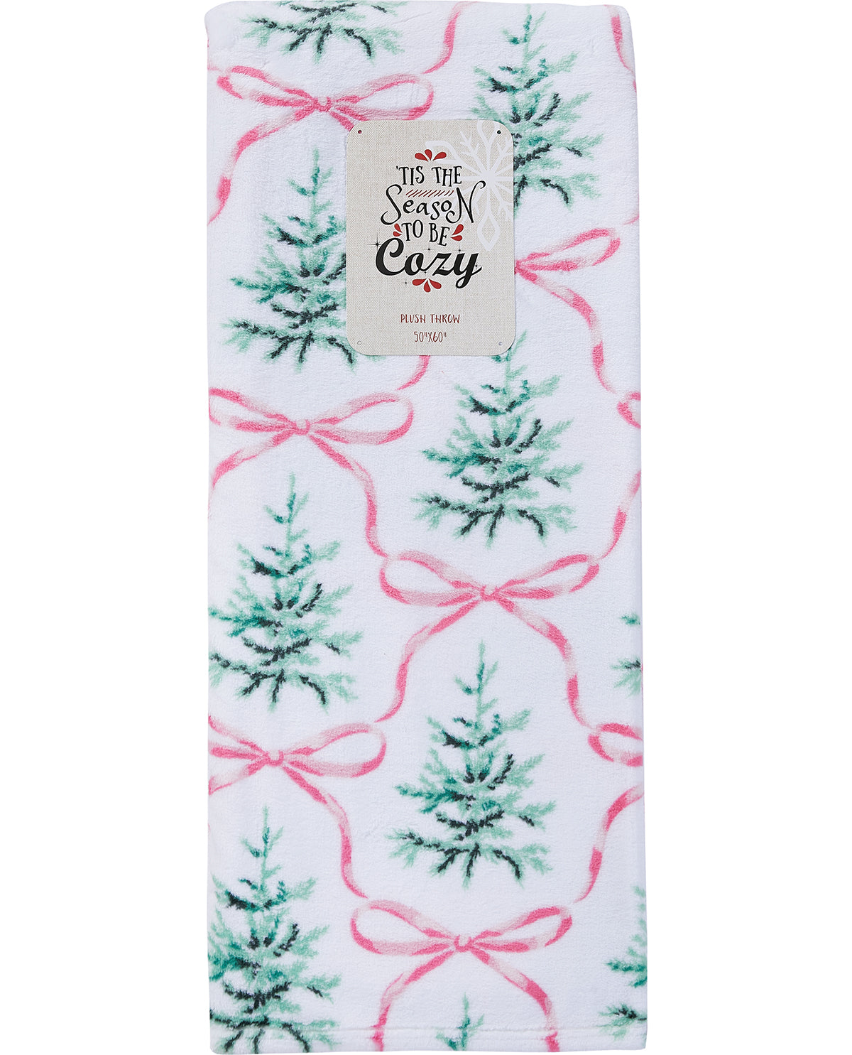 A folded white blanket featuring a festive Christmas pattern of green pine trees and pink ribbon bows, with a paper label attached at the top that reads 'To the Season to be Cozy'.