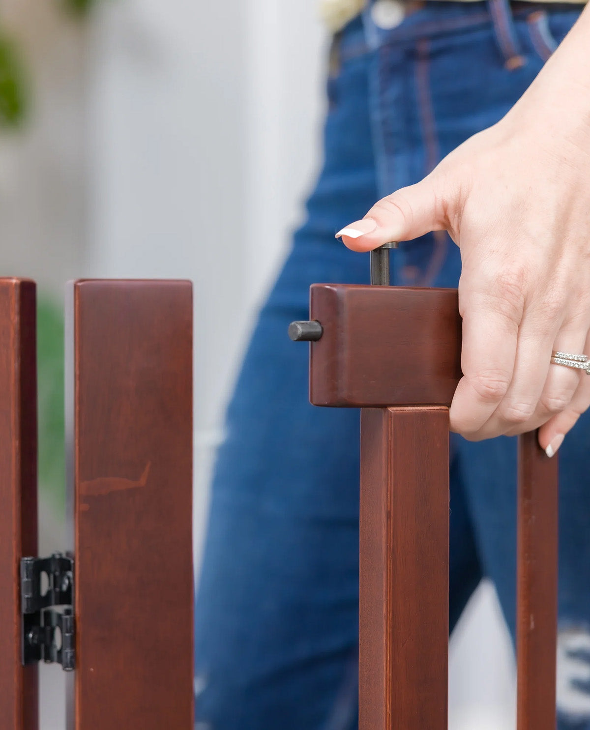 A close-up of a person's hand adjusting a metal latch on a brown wooden gate, with blue jeans visible in the background.
