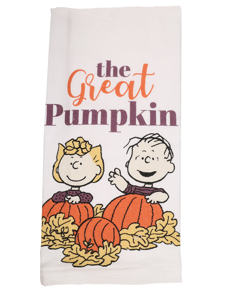 A white kitchen towel featuring a Peanuts autumn graphic with the text 'the Great Pumpkin' and Charlie Brown and Snoopy sitting in pumpkins among yellow leaves.