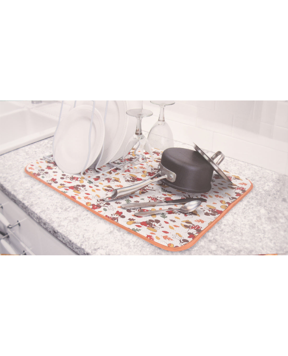 Floral-patterned mat on a kitchen counter with utensils and a pot lid.