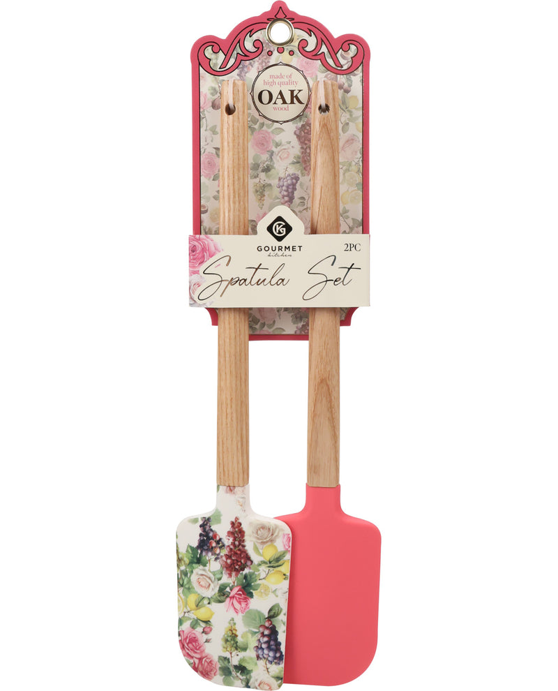 A 2-piece Gourmet Oak spatula set in retail packaging, featuring one floral-patterned spatula and one solid coral pink silicone spatula with wooden handles.