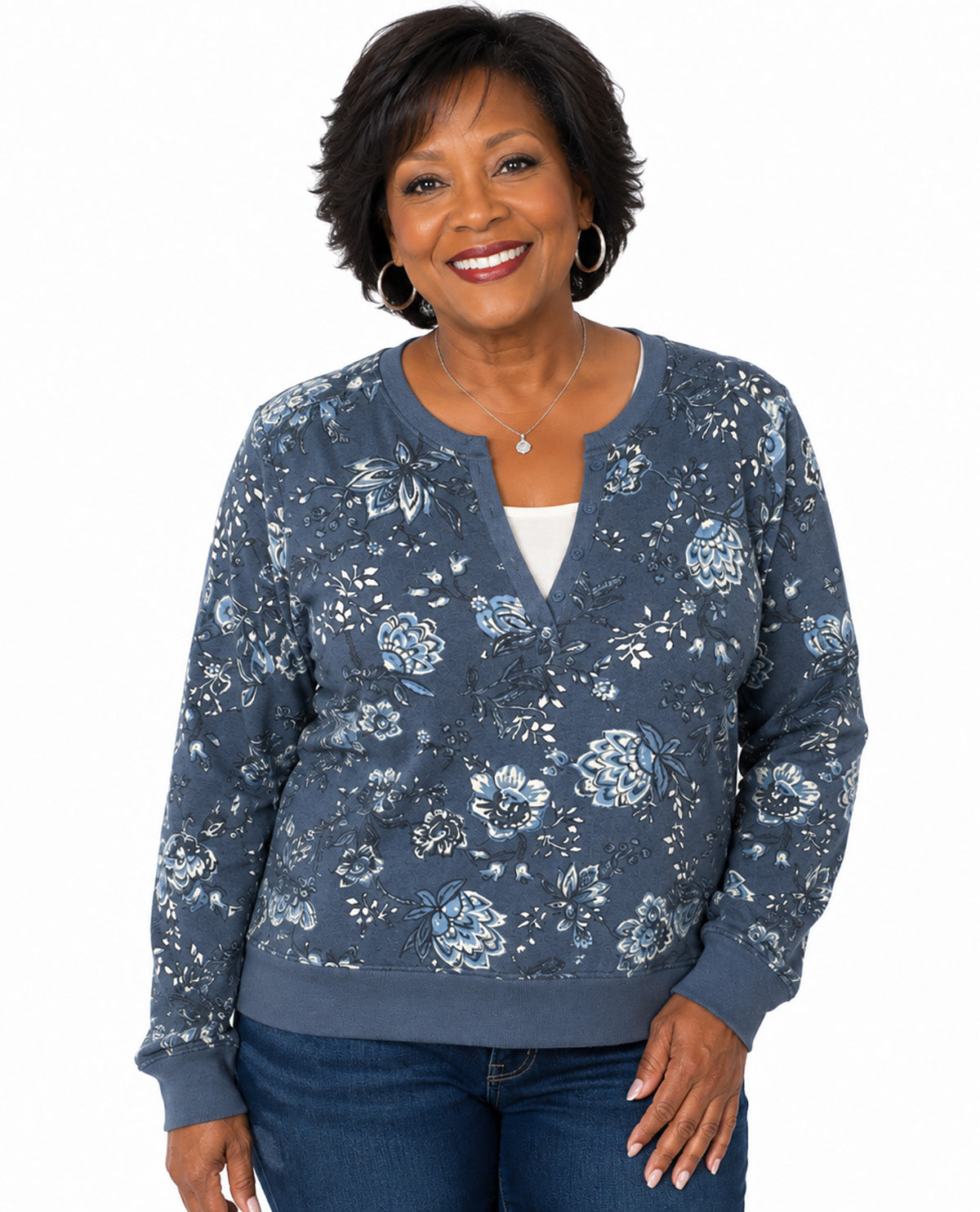 A smiling woman with short dark hair models a slate blue floral long-sleeve cardigan over a white top and blue jeans, set against a plain white background.