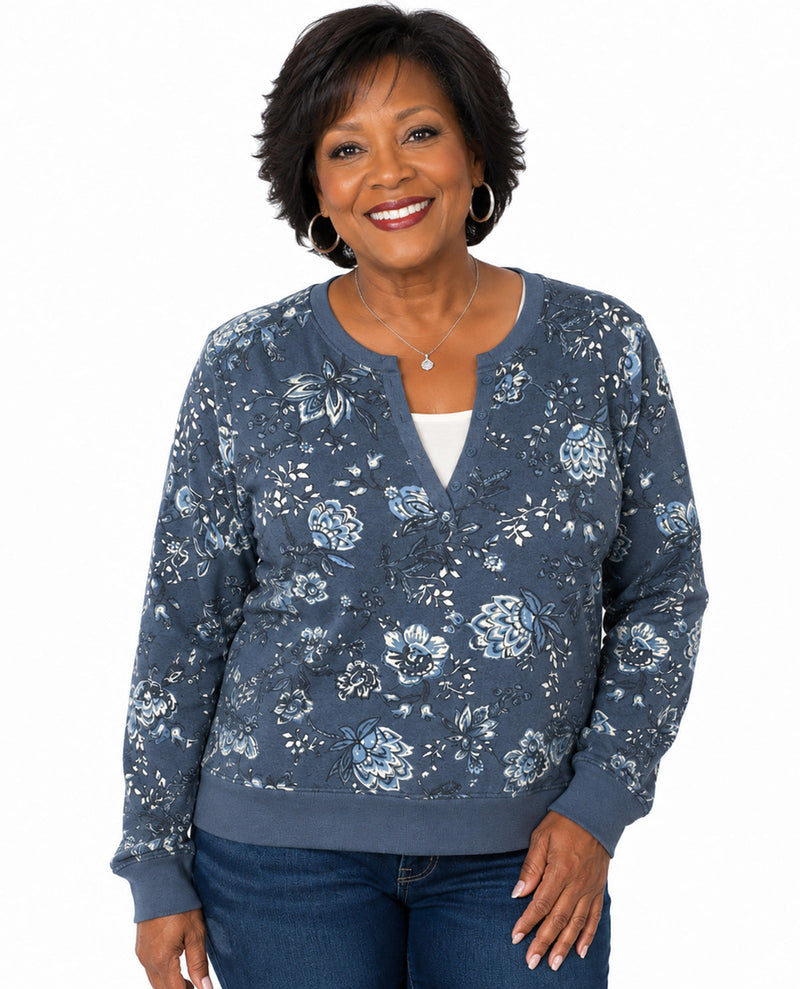 A smiling woman with short dark hair models a slate blue floral long-sleeve cardigan over a white top and blue jeans, set against a plain white background.