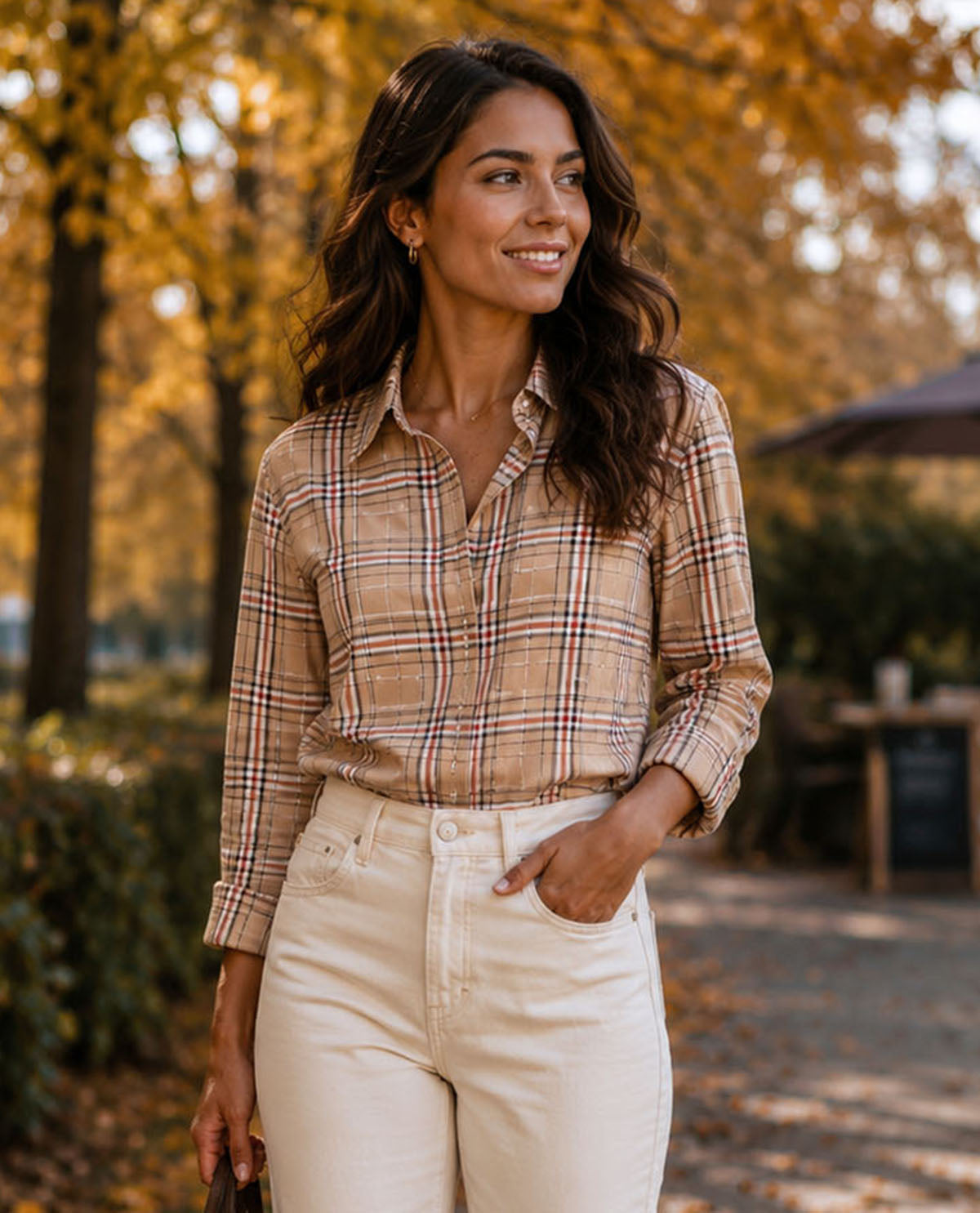 Woman wearing a plaid shirt and white pants standing in an autumn setting.