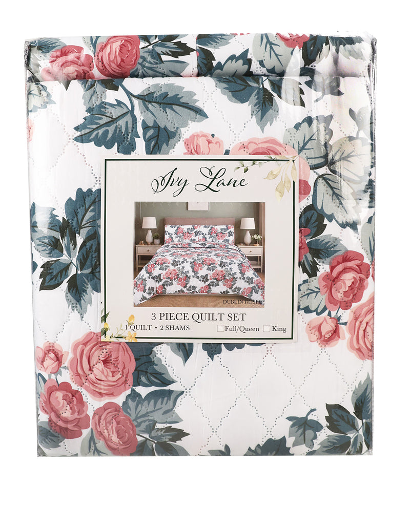 A packaged 3-piece quilt set by Sly Lane, featuring a white background with a pink rose and blue-gray floral pattern and a central label showing the quilt styled on a bed.