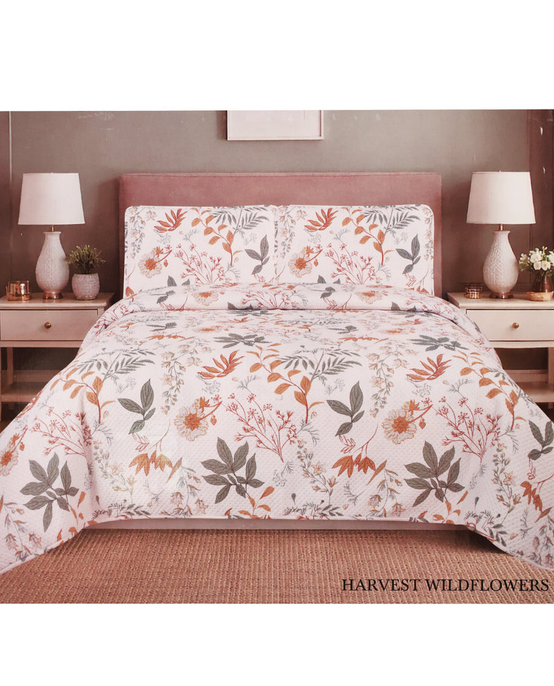 A floral comforter and matching pillow shams displayed on a bed in a styled bedroom setting. The pattern features orange, brown, and gray wildflower botanical motifs on a white background.