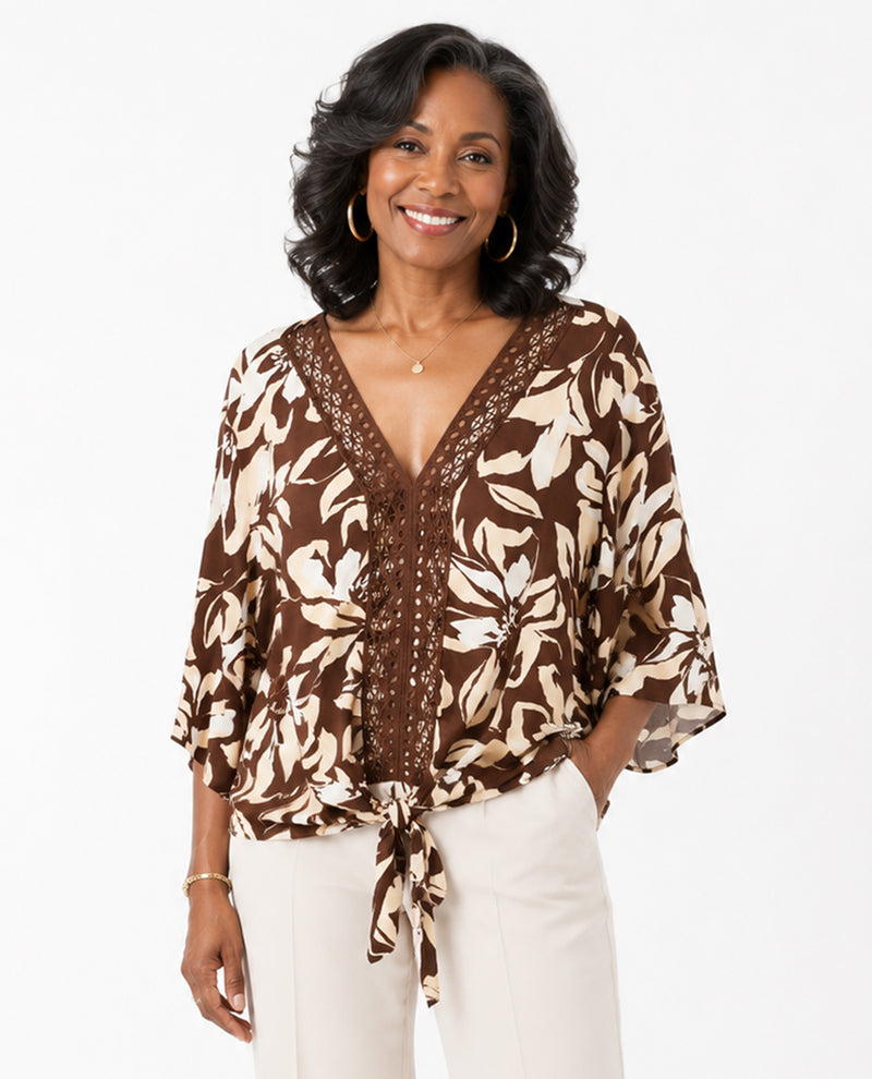 Woman wearing a brown floral blouse with white pants on a white background