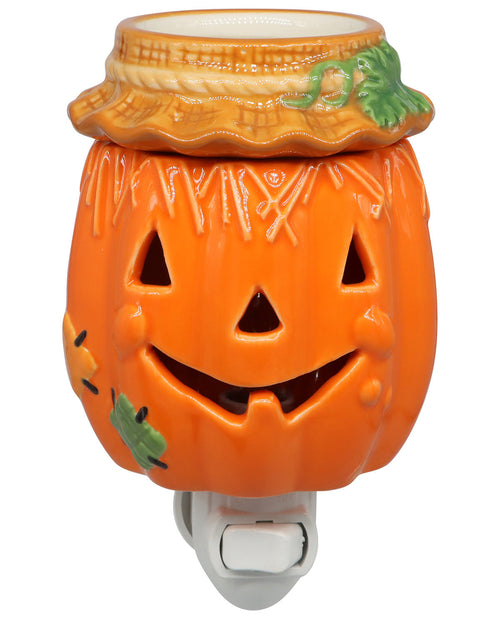 An orange ceramic jack-o'-lantern night light or diffuser with a smiling carved face, decorative stem details, small green leaf accents, and a white plastic plug at the bottom, shown on a plain white background.