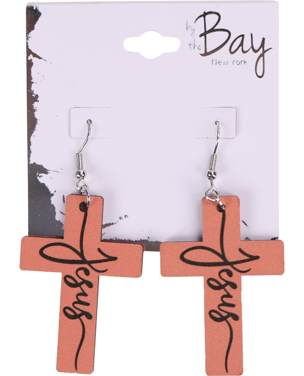 A pair of cross-shaped dangle earrings in a terracotta pink color with the word 'Jesus' written in black script, displayed on a white 'by the Bay New York' retail card.